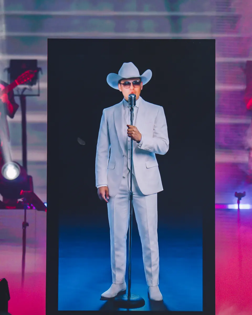 Avatar de Yeison Jiménez en traje blanco cantando en pantalla LED, luces rosadas y azules
